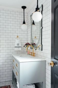 a white bathroom with black and gold fixtures on the vanity, mirror and lights above it