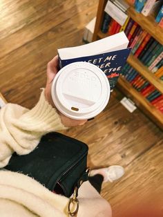 a person holding a coffee cup and book in front of a bookshelf full of books