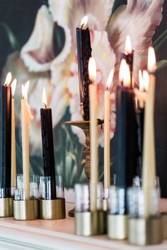 candles are lined up on a mantle with flowers in the background