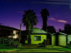 a green house with palm trees in the front yard at night, and a full moon behind it