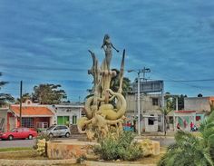 a statue in the middle of a street with cars and buildings behind it on a cloudy day