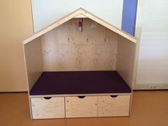 a wooden shelf with two drawers and a purple cushion on it's bottom half