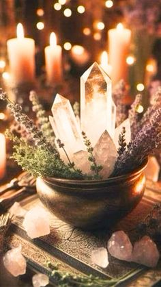 crystals and greenery in a bowl on a table surrounded by candles, rocks and other items