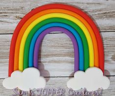 a rainbow shaped cookie sitting on top of a wooden table next to a sign that says san's topper creations