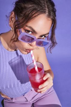 a woman with glasses holding a drink in her hand and drinking it from a straw