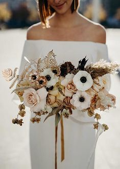 a woman in white dress holding a bouquet of flowers on her arm and wearing an off the shoulder wedding dress