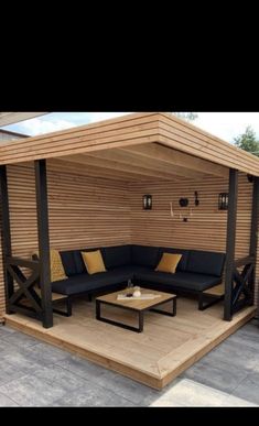 a wooden gazebo with black and yellow cushions on it's sides, in the middle of a patio