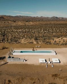 an aerial view of a swimming pool in the middle of desert with people sitting around it