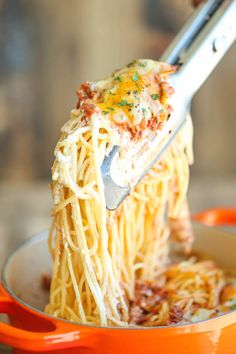 someone is holding a fork full of spaghetti with sauce and cheese on it in an orange pan