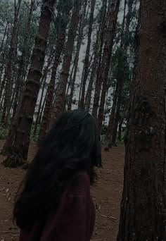 a woman standing in the woods looking up at trees