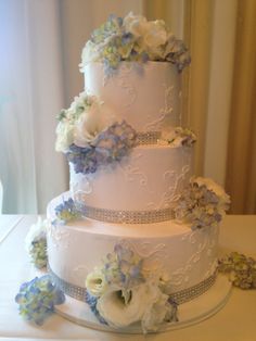 a three tiered wedding cake with blue and white flowers