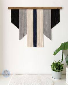 the wall hanging is decorated with black, white and grey fringes next to a potted plant