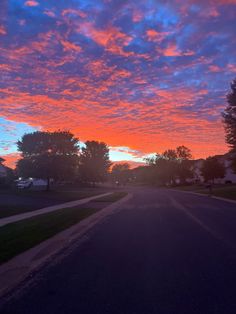 the sun is setting over an empty street with houses in the distance and trees on either side