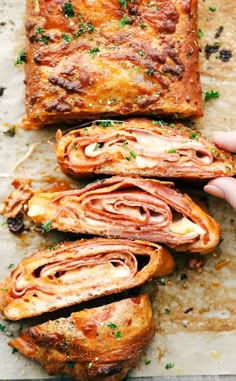 someone is holding up some bread with meat and cheese in it on a sheet of baking paper