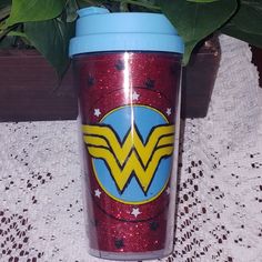 a wonder woman logo on a red glitter tumbler next to a potted plant