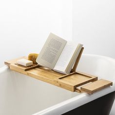 an open book is sitting on the edge of a bathtub with a wooden tray