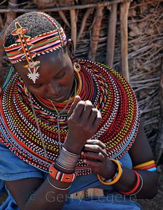 a woman sitting in front of a hut holding her hands together