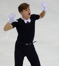 a male figure skater in a black shirt and white gloves is performing on the ice