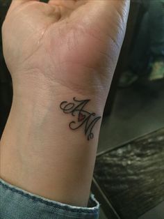 a woman's wrist tattoo with the letter m in cursive writing on it