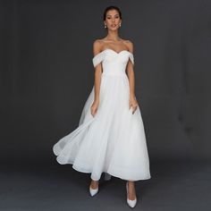 a woman wearing a white wedding dress and high heeled shoes standing in front of a gray background