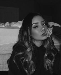 a woman with long hair sitting in front of a bed and looking at the camera