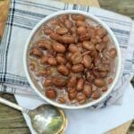 a white bowl filled with beans on top of a wooden table next to a spoon