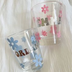 two glass cups sitting next to each other on a white surface with flowers painted on them