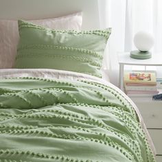 a bed with green comforter and pillows in a room next to a white nightstand