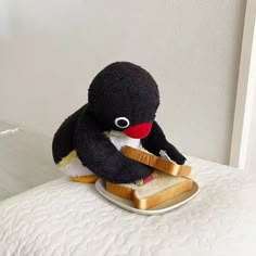 a stuffed penguin sitting on top of a plate with bread in it's mouth