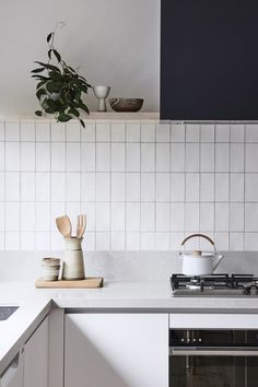 a kitchen with white tiles and wooden utensils on the counter top, next to a potted plant