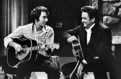 two men sitting next to each other playing guitars