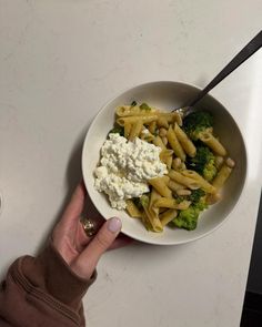 a person is holding a spoon over a bowl of pasta with broccoli and feta