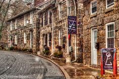 a cobblestone street lined with stone buildings in the wintertime, with snow falling on the ground