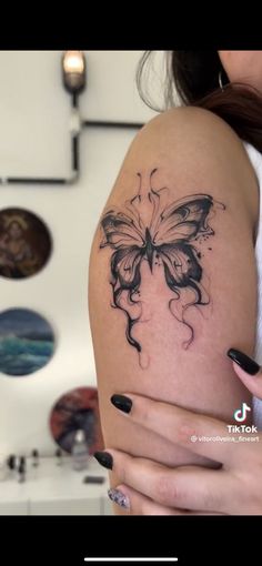 a woman holding her arm with a butterfly tattoo on it's left side shoulder