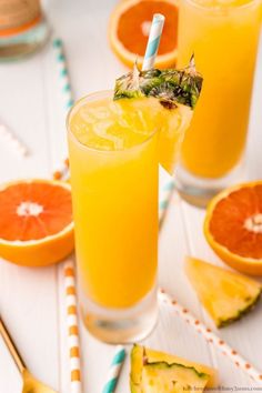 two glasses filled with orange juice next to slices of pineapple and an orange slice