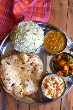 a metal plate topped with rice and different types of food on top of a wooden table