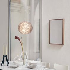 a dining room table with white chairs and a vase on top of it, in front of a mirror