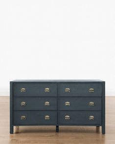 a black dresser with gold handles and drawers on top of wooden floors in front of a white wall