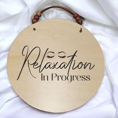 a wooden sign that says relaxation in progress on white fabric with beaded string hanging from it