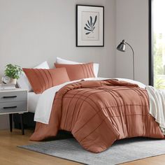 a bed with an orange comforter and white sheets in a room next to a window