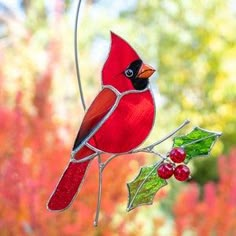 a red bird sitting on top of a tree branch next to a green berry and leaf