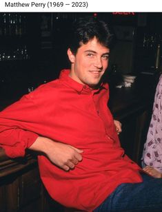 a man in a red shirt sitting at a bar with his arm around another man's shoulder