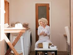 a woman with blonde hair sitting on a stool next to a washer and dryer