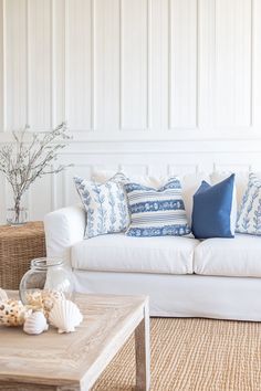 a white couch with blue and white pillows on top of it next to a coffee table