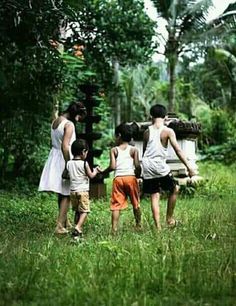 three children are walking in the grass with their mother and father, who is holding hands