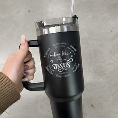 a person holding a black coffee cup with the words jesus on it and a straw in their hand