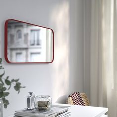 a white table topped with magazines and a red mirror on the wall next to a window