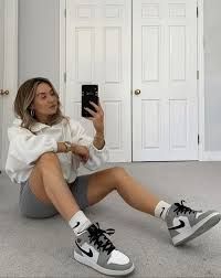 a woman sitting on the floor taking a selfie with her cell phone while wearing nike sneakers