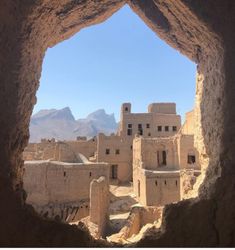 the view from inside a cave looking out at an old village with mountains in the background