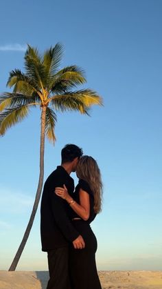 a man and woman standing next to each other on a beach under a palm tree